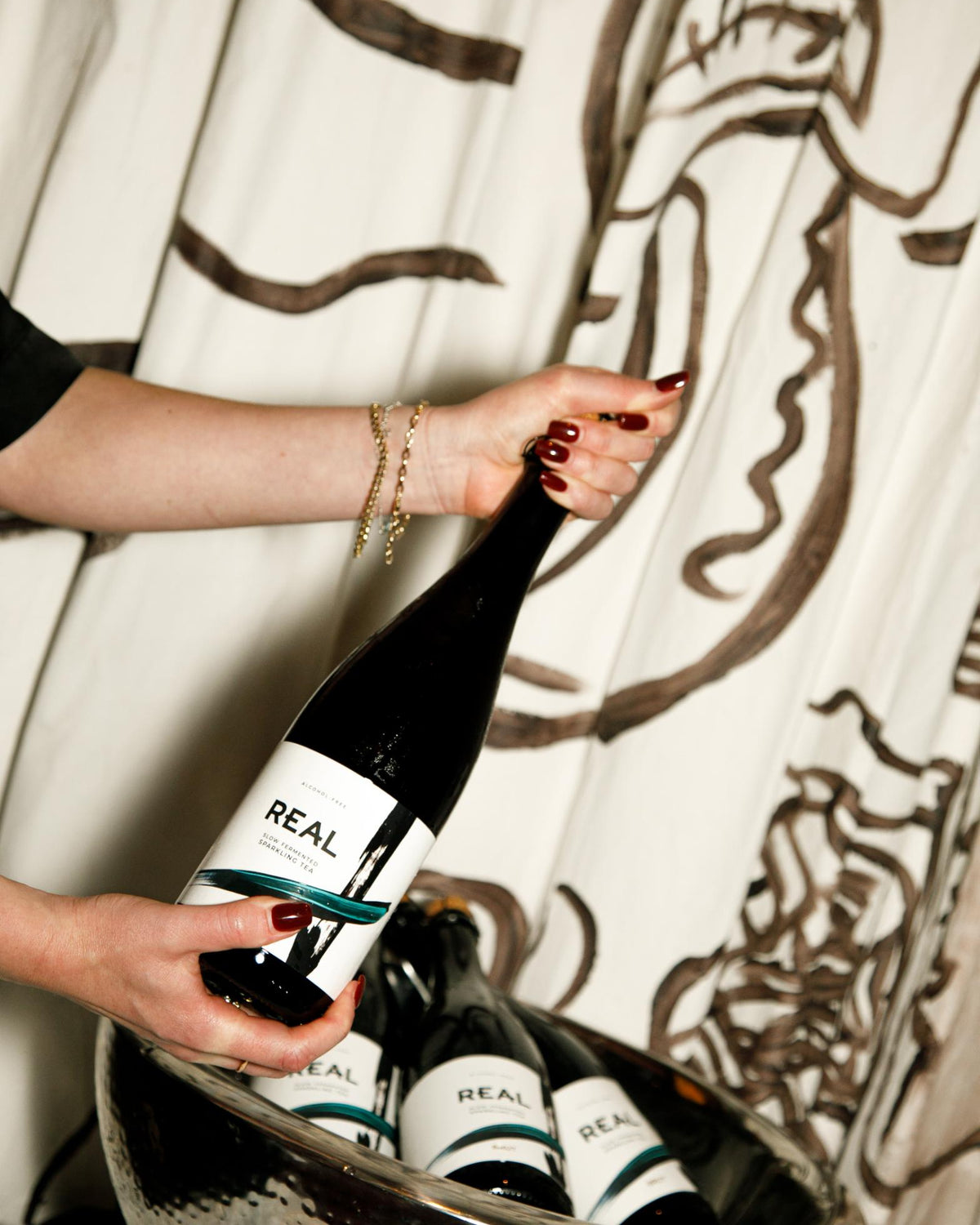 Hands holding a bottle of REAL Brut, with more bottles in an ice bucket below