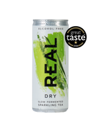 A silver aluminum can of REAL Dry Slow Fermented Sparkling Tea, featuring a vibrant green paint stroke design and a black vertical 'REAL' logo. A black 'great taste 2026' award badge is displayed in the upper right corner.