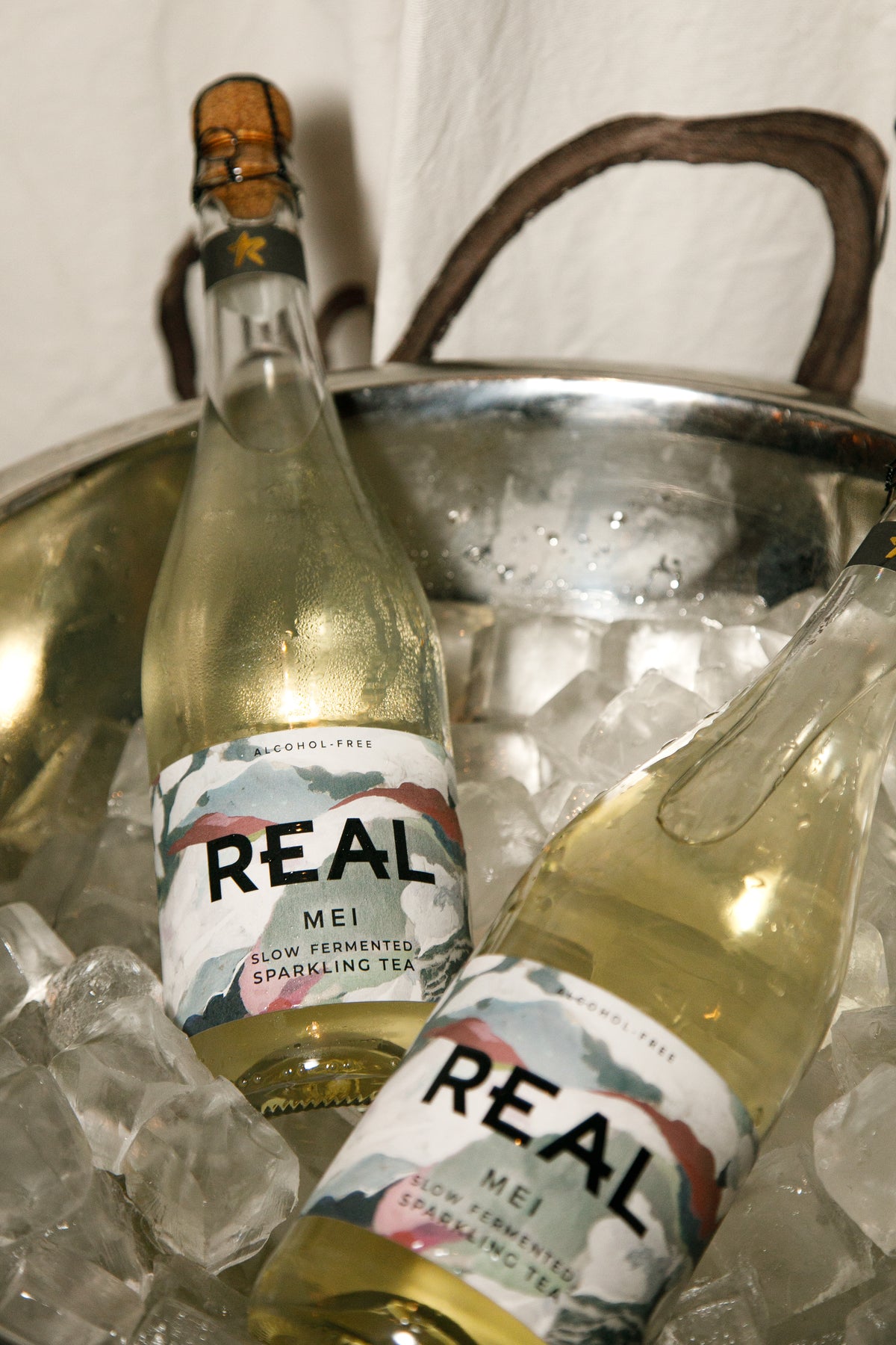 Two bottles of REAL Mei slow fermented sparkling tea resting in a metal bucket filled with ice.