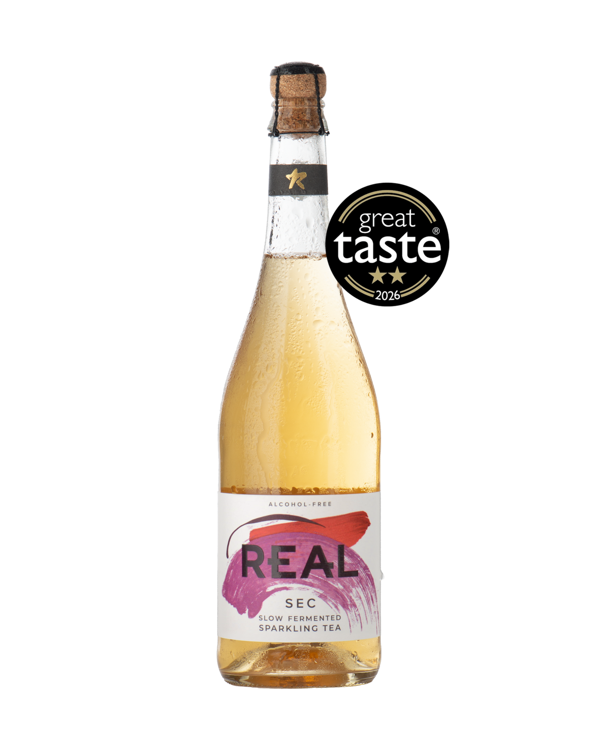 A bottle of REAL Sec alcohol-free sparkling tea with a cork stopper, filled with a light pink liquid, featuring a white and purple label. A black 'great taste 2026' award badge is overlaid on the upper right side of the bottle.