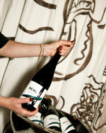 Hands holding a bottle of REAL Brut, with more bottles in an ice bucket below