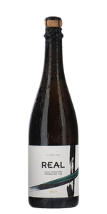 A dark glass bottle of REAL brand non-alcoholic slow fermented sparkling tea, Brut, with a cork stopper and a white label featuring black and green graphic elements, set against a plain white background.