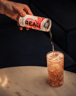 Person pouring a drink'REAL' into a glass on a marble surface.