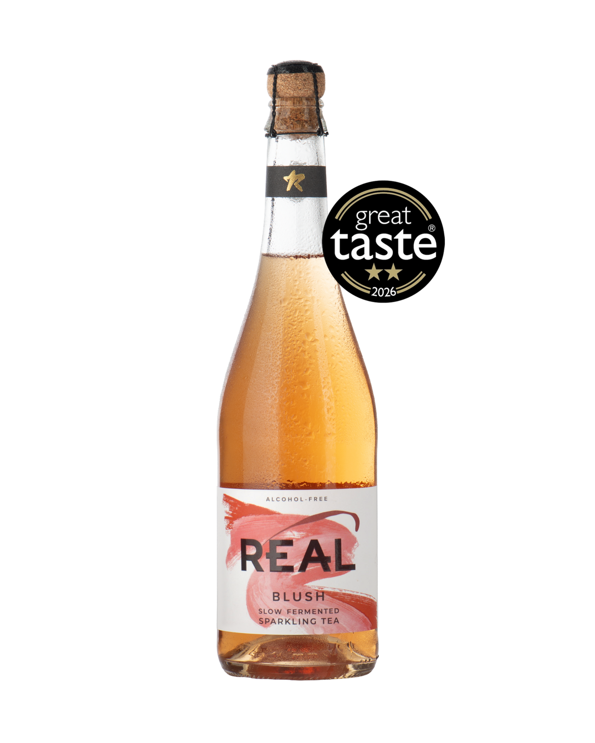 A bottle of REAL BLUSH alcohol-free sparkling tea with a cork stopper, filled with a pinkish-rose liquid, featuring a white and pink label. A black 'great taste 2026' award badge is overlaid on the upper right side of the bottle.