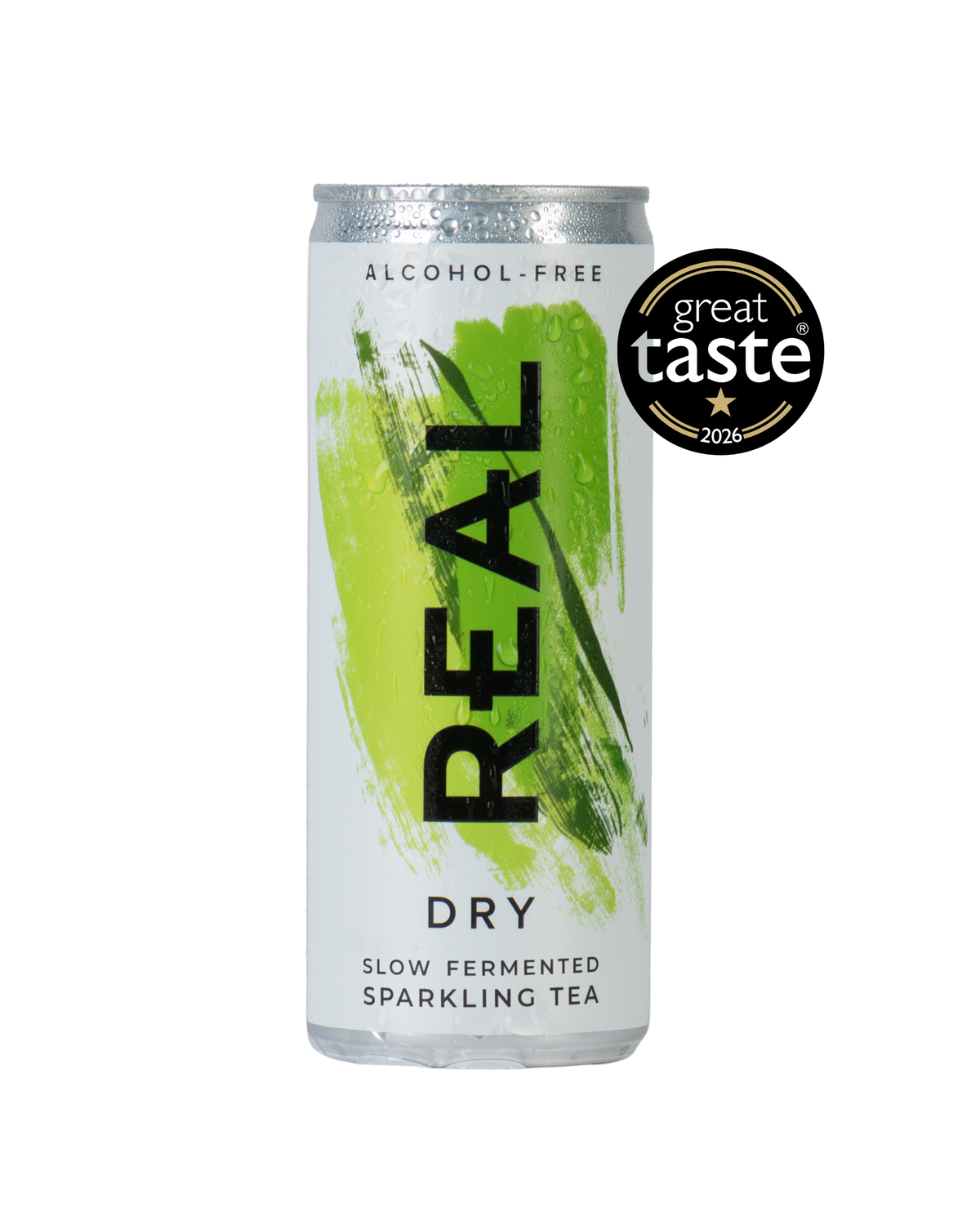 A silver aluminum can of REAL Dry Slow Fermented Sparkling Tea, featuring a vibrant green paint stroke design and a black vertical 'REAL' logo. A black 'great taste 2026' award badge is displayed in the upper right corner.